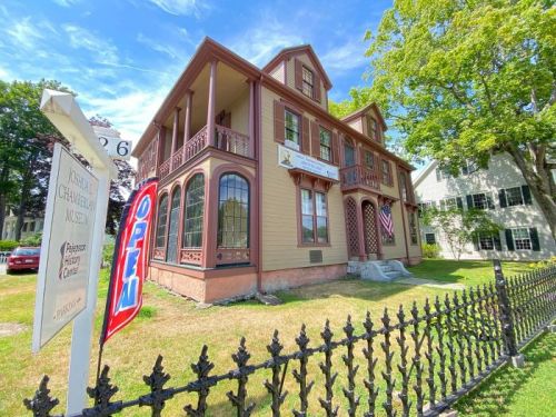 Historic building with a sign reading "Open," surrounded by a black iron fence and green grass under a blue sky.