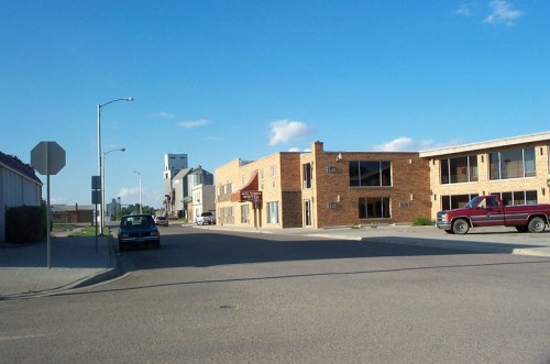A street view featuring brick buildings, a stop sign, and parked cars under a clear blue sky.