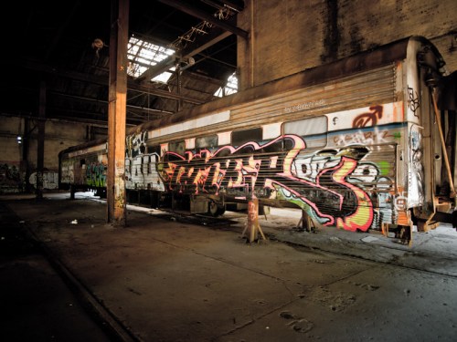 Abandoned train cars covered in vibrant graffiti inside a dilapidated warehouse.