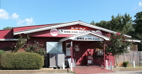 Exterior of Dreamland BBQ restaurant, featuring a red building with signage and a landscaped entrance.