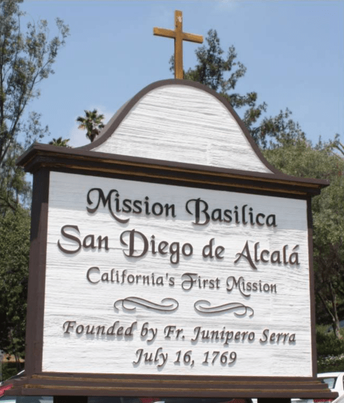 Sign for Mission Basilica San Diego de Alcalá, California's first mission, founded July 16, 1769. Cross on top.