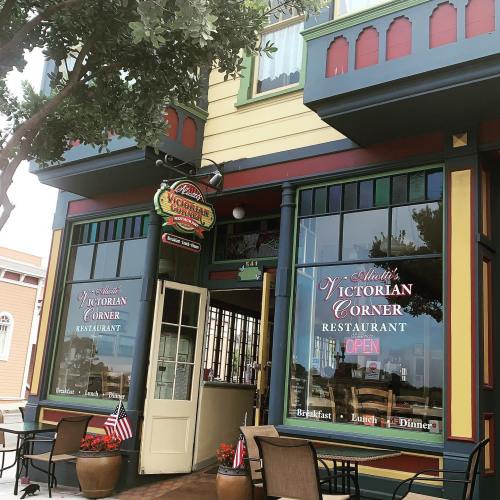 Exterior of Victorian Corner Restaurant with colorful architecture, open sign, and outdoor seating.