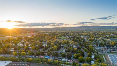 Aerial view of a town at sunset, with green trees and houses spread across the landscape under a colorful sky.