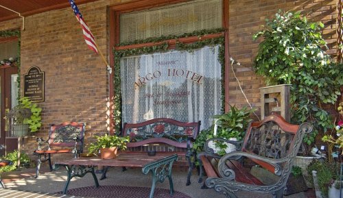 Historic hotel entrance with benches, plants, and an American flag, featuring a decorative window sign.