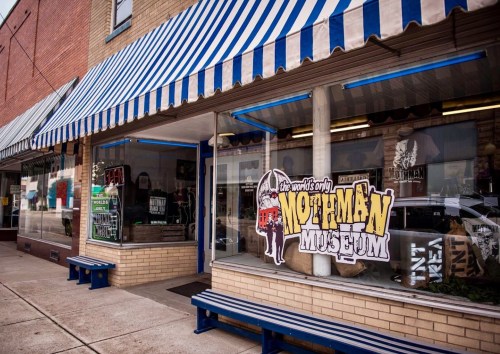 Exterior of the Mothman Museum, featuring a colorful awning and a large sign, with merchandise displayed in the windows.