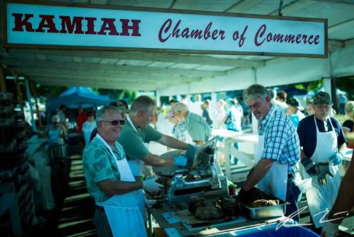 A busy outdoor market scene with people serving food at the Kamiah Chamber of Commerce booth.