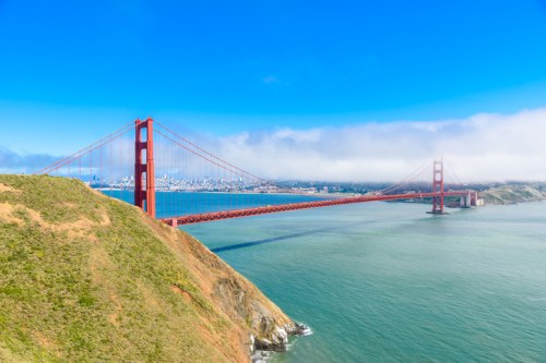 Golden Gate Bridge spanning a bay, with a clear blue sky and distant city skyline in the background.