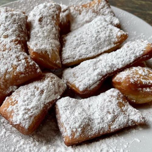 A plate of golden-brown pastries dusted with powdered sugar, arranged neatly.