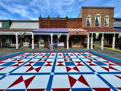 Colorful quilt-patterned pavement in front of historic buildings under a blue sky.