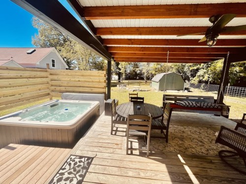 A patio with a hot tub, dining table, and chairs, surrounded by wooden fencing and a shed in the background.