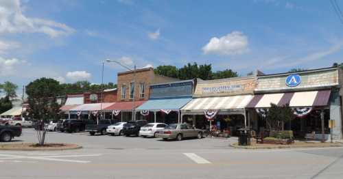 A charming small-town street with historic buildings, shops, and parked cars under a blue sky with fluffy clouds.