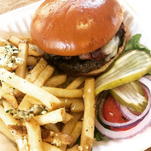 A juicy burger with bacon and cheese, served with crispy fries, pickles, and fresh vegetables on the side.