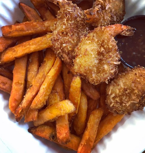 A bowl of golden-brown sweet potato fries and crispy coconut shrimp with a side of dipping sauce.