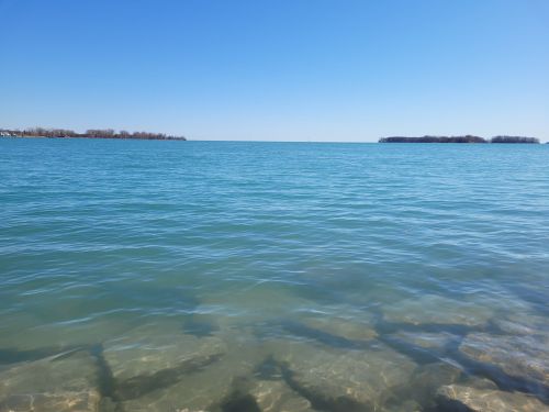 A calm blue lake under a clear sky, with distant islands visible on the horizon.