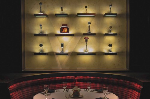 A dimly lit wall display featuring vintage microphones and an "ON AIR" sign above a round dining table.
