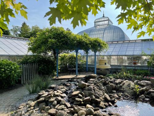 A serene garden scene featuring a rock pond, a gazebo, and a greenhouse under a clear blue sky.