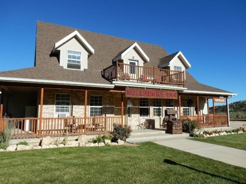A charming two-story inn with a porch, surrounded by greenery and a clear blue sky.