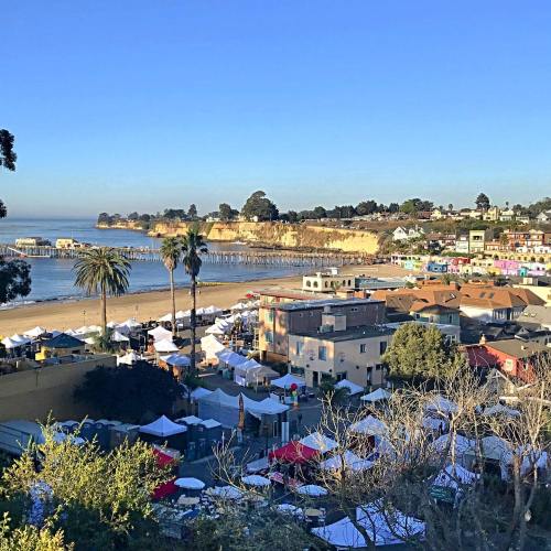 A coastal view of a beach with colorful buildings, palm trees, and tents set up for an event under a clear blue sky.