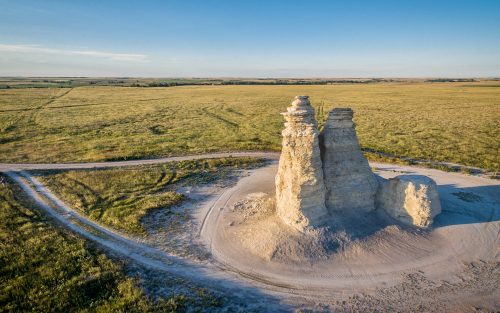 Aerial view of a tall rock formation surrounded by open grassland under a clear blue sky.