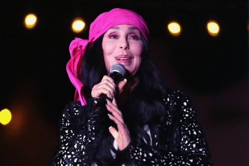 A woman with long black hair and a pink headscarf smiles while holding a microphone on stage.