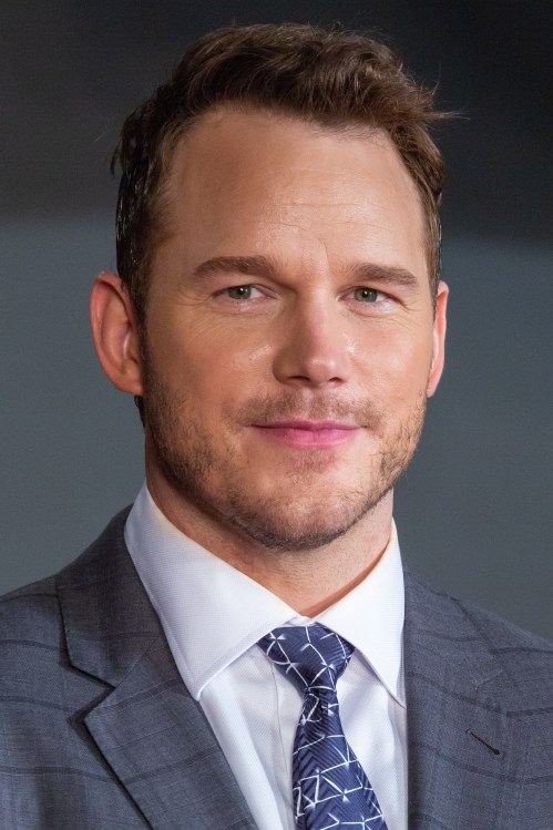 A man in a suit with a tie, smiling confidently at the camera, with short, styled hair and a well-groomed appearance.