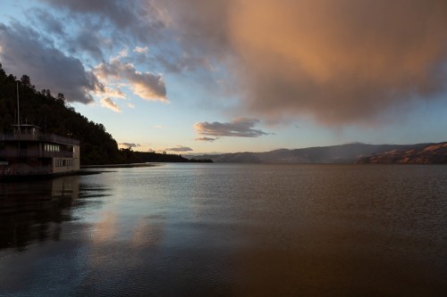 A serene lake at sunset, with clouds reflecting on the water and mountains in the distance.
