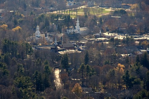 Aerial view of a small town with churches, trees, and a sports field in the background during autumn.