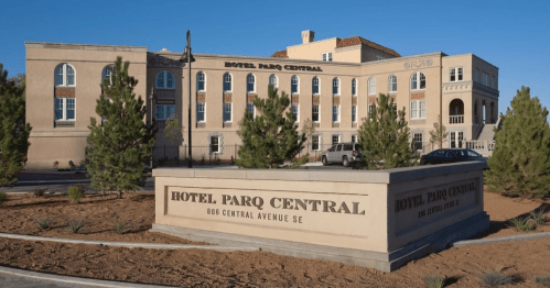 Exterior view of Hotel Parq Central, featuring a sign and landscaped area with trees and shrubs.