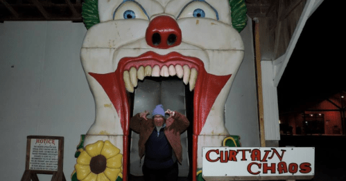 A person stands in front of a large clown entrance, making a playful gesture, with a sign reading "Curtain Chaos."