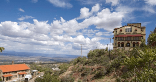 A scenic view of a hillside with a hotel and a distant landscape under a partly cloudy sky.