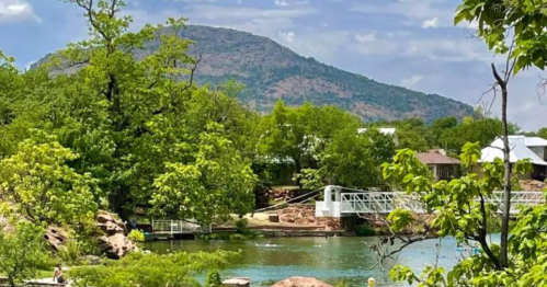 Scenic view of a lake surrounded by lush greenery and a mountain in the background under a partly cloudy sky.