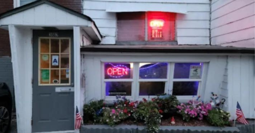 A small building with an "OPEN" neon sign and flower beds, decorated with small American flags.