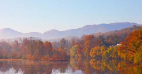 A serene autumn landscape with colorful trees reflecting on a calm lake, surrounded by misty mountains.