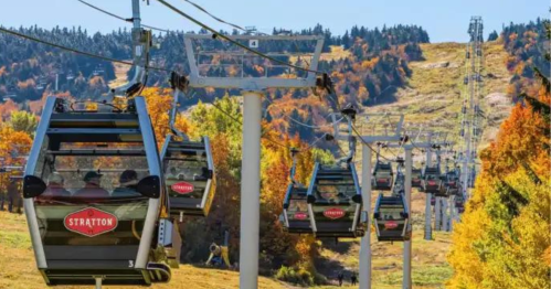 A row of gondolas on a ski lift with colorful autumn foliage in the background at Stratton Mountain.