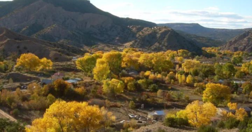 A scenic view of a valley with vibrant yellow trees, surrounded by mountains under a clear blue sky.