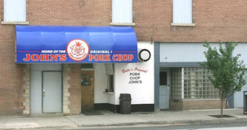 Exterior of a restaurant with a blue awning reading "John's Original Pork Chop" and a brick building facade.