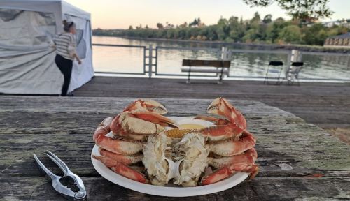 A plate of crabs on a wooden table by a river, with a person in the background and a tent nearby.