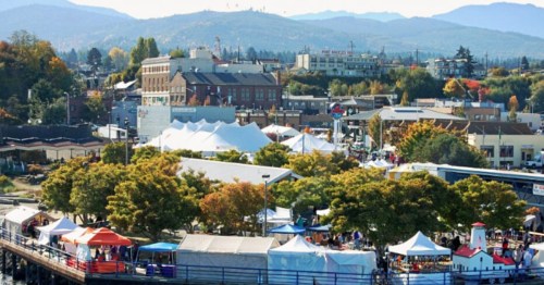 Aerial view of a vibrant outdoor market with tents, surrounded by trees and mountains in the background.