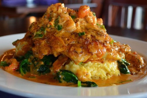 A plate of creamy shrimp and grits topped with sautéed shrimp and green onions, served on a wooden table.