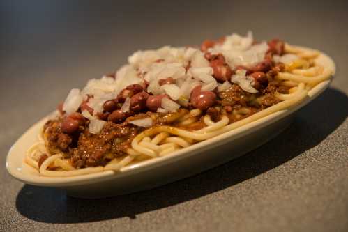 A plate of spaghetti topped with chili, kidney beans, and chopped onions, served on a light-colored dish.