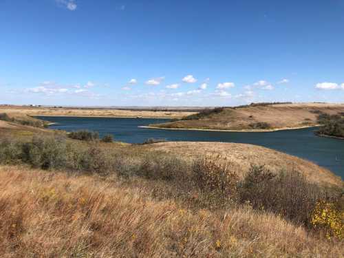 A serene landscape featuring a winding river surrounded by grassy hills and a clear blue sky with scattered clouds.