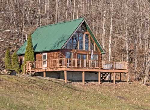 A cozy wooden cabin with a green roof, surrounded by trees and featuring a spacious deck.