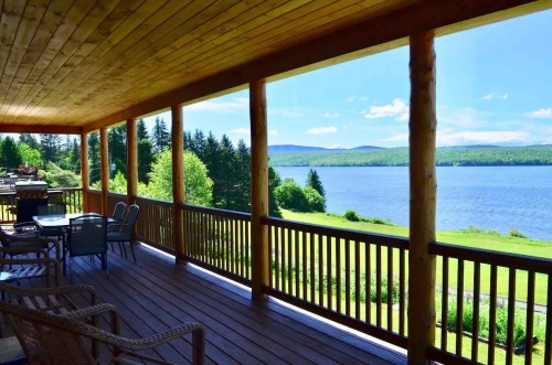 A scenic view from a wooden porch overlooking a lake and green hills under a clear blue sky.