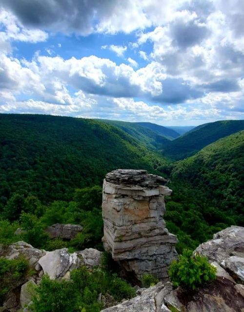 A rocky outcrop stands prominently against a lush green valley and a blue sky filled with fluffy clouds.