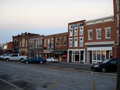 A quiet street scene featuring historic brick buildings and parked cars in a small town.