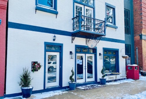 A charming white building with blue accents, featuring a balcony, potted plants, and a small outdoor seating area.