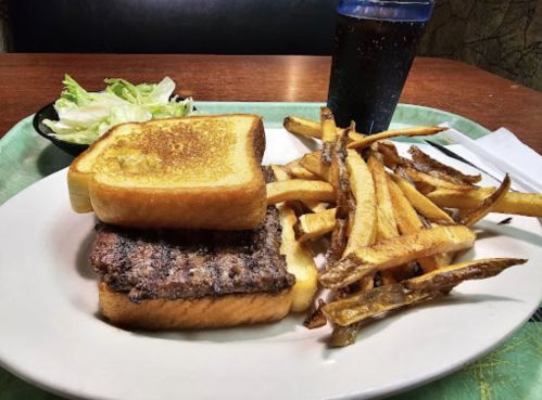 A plate with a burger on toast, fries, and a side salad, accompanied by a drink in a cup.