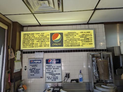 Menu board in a diner featuring food items, prices, and Pepsi branding, with a clean, retro interior.