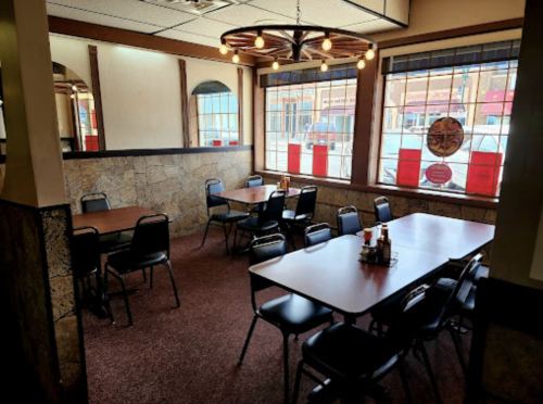 A cozy restaurant interior with tables, chairs, and large windows featuring red decorations and a warm light fixture.