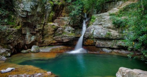 A serene waterfall cascades into a tranquil pool, surrounded by lush greenery and rocky cliffs.